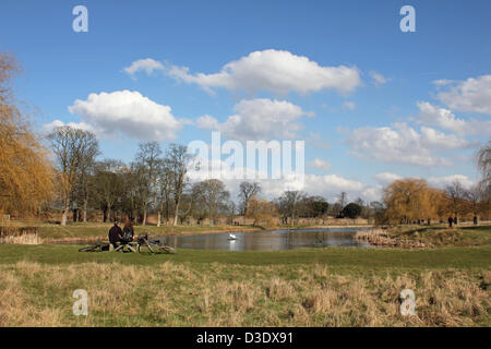 17 febbraio 2013, Hampton Court, Inghilterra, Regno Unito. I ciclisti una sosta per gustare glorioso sole primaverile e la vista su tutta la Hampton Wick stagno all'interno di Hampton Court Park (Home Park) murata Deer Park di circa 700 acri. Foto Stock