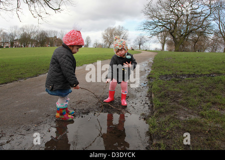 Il Toddler due gemelle a giocare nelle pozzanghere nel park REGNO UNITO Foto Stock