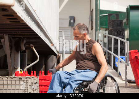 Banchina di carico lavoratore con lesioni al midollo spinale in una sedia a rotelle di impilamento dei vassoi di inventario Foto Stock