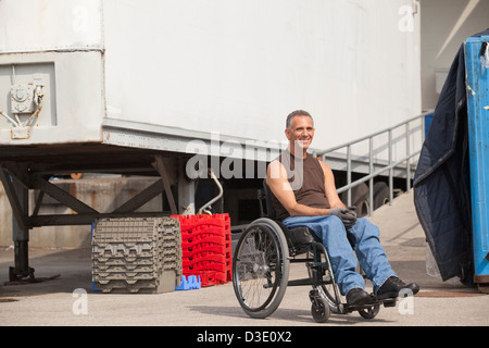 Banchina di carico lavoratore con lesioni al midollo spinale in una sedia a rotelle in area di storage Foto Stock