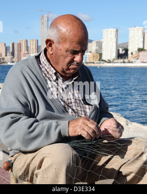 Il vecchio uomo riassettavano le reti da pesca nel porto di Benidorm Spagna Foto Stock