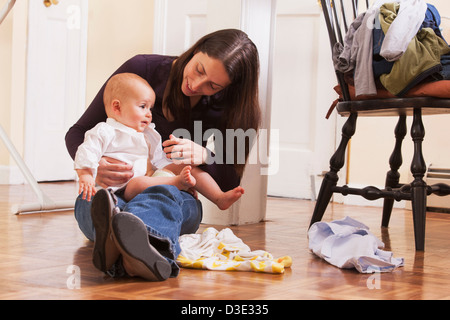 Cambiando la madre del suo figlio vestiti mentre è seduto sul pavimento Foto Stock