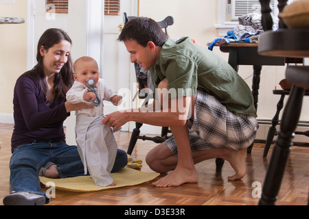 I genitori cambiando il loro figlio gli abiti insieme mentre è seduto sul pavimento Foto Stock