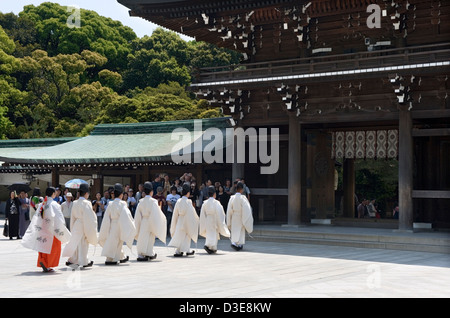 Lo Shintoismo sacerdoti e una miko maiden in un abito rosso in processione attraverso il cancello principale di Meiji Jingu durante una cerimonia religiosa Foto Stock