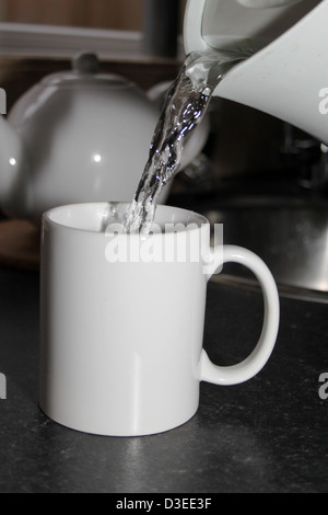 Acqua bollente versata da un bollitore in una tazza bianca Foto Stock