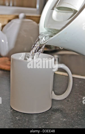 Acqua bollente versata da un bollitore in una tazza bianca Foto Stock
