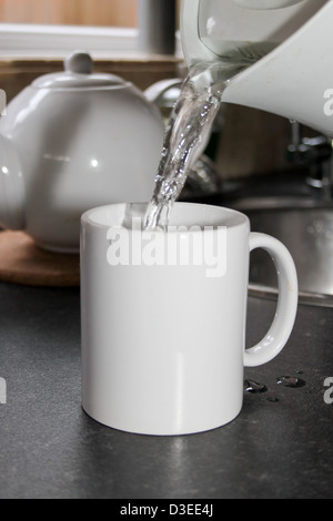 Acqua bollente versata da un bollitore in una tazza bianca Foto Stock