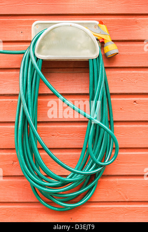 Il verde giardino di plastica flessibile e ugello appeso alla parete di un rosso casa in legno Foto Stock