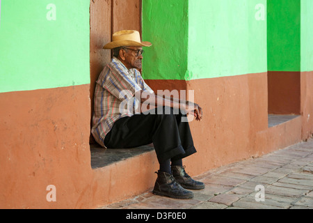 Ritratto di vecchio uomo cubano seduti di fronte color pastello davanti casa per le strade di Trinidad, Cuba Foto Stock