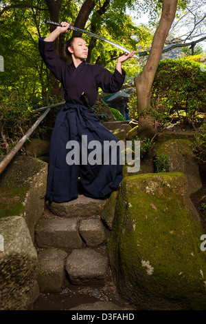 Un Samurai Warrior sorge in un tradizionale giardino tenendo una spada katana. Foto Stock