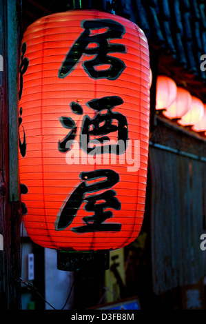 Red chochin lanterna di carta con i caratteri kanji "Izakaya,' casual stabilimento potabile popolare con dopo-lavoro la folla in Giappone Foto Stock