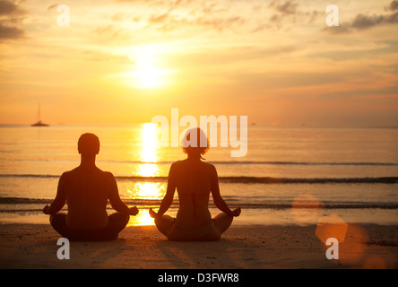 Una coppia giovane seduto sulla spiaggia del mare nella posizione del loto al tramonto. La pratica dello yoga. Foto Stock