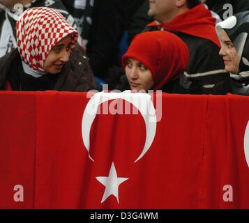 (Dpa) - Femmina Turkish soccer fans sedere in tribuna dietro il Bagno Turco bandiera nazionale durante la European Champions League gioco di gruppo del Chelsea Londra contro Besiktas Istanbul a Gelsenkirchen (Germania), 9 dicembre 2003. Chelsea ha vinto il gioco 2-0 ed entra nel giro di 16 come gruppo vincitore. Istanbul è eliminato. Il gioco è stato spostato da Istanbul per la Germania a causa del recente Foto Stock