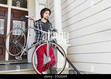 Hipsters e beatnik - un giovane uomo tanga in jeans stretti, plaid shirt e hat circa per lasciare la casa nel suo fixed-gear bike. Foto Stock