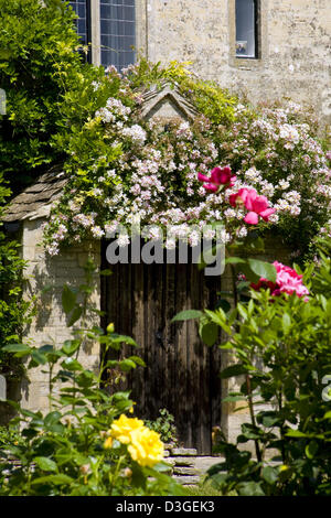 Un vecchio cottage in pietra con rose rampicanti oltre la porta Gloucestershire, England, Regno Unito Foto Stock