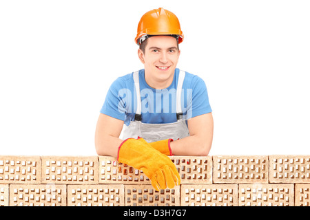 Maschio lavoratore edile in appoggio su una parete di mattoni isolati su sfondo bianco Foto Stock