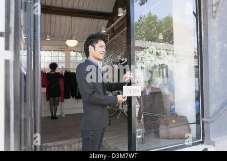 Nuova generazione di imprenditore cinese, mettendo su 'aperto' firmare alla porta del suo negozio nel quartiere di Dong Cheng a Pechino Foto Stock