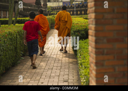 Due monaci buddisti e un ragazzo di camminare lungo un percorso di mattoni fra il verde delle siepi. Foto Stock