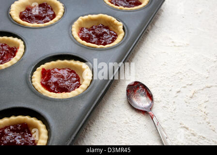 Riempito, non cotti crostate di frutta in una teglia con una jam-coperto cucchiaino accanto Foto Stock