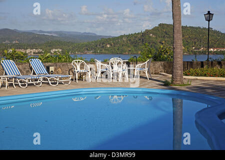 Sedie a sdraio blu lungo la piscina di Hotel El Castillo con vista sulla baia di mare dei Caraibi a Baracoa, Cuba Foto Stock