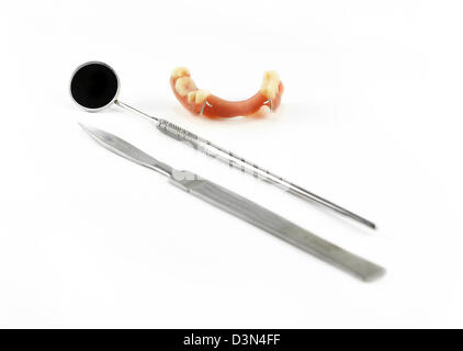 Dentiera parziale accanto a bisturi e specchio dentale, isolato su bianco Foto Stock