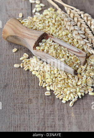 Cucchiaio di legno riempita di grani di grano su grano dispersi Foto Stock