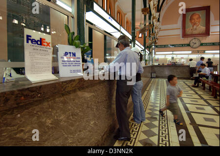 Un uomo di spunti a una scrivania la Posta centrale di Ho Chi Micnh City, Vietnam, 24 febbraio 2006. La camera dispone di un segno di noi azienda logistica FedEx e una foto di ex leader del Vietnam, Ho Chi Minh. Foto: Christine Kokot Foto Stock