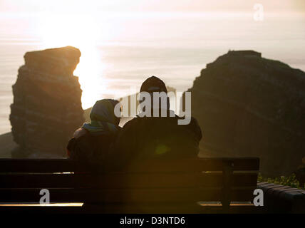 Un giovane si siede su un banco e si affaccia su un 47 metri di altezza con pietra arenaria rossa rock 'Lange Anna" (Tall Anna) durante il tramonto sul piccolo arcipelago Helgoland, Germania, 10 giugno 2006. Il free-standing rock è l'isola di Helgoland è più popolare punto di riferimento. Un ex danesi e britannici possesso, le isole (popolazione 1.650) sono situati nell'isola di Helgoland ansa o Bight tedesco nel sud-est cor Foto Stock