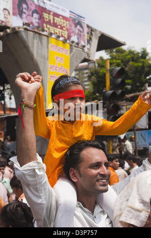 Uomo che porta la sua figlia sulle sue spalle alla processione religiosa durante Ganpati visarjan cerimonia, Mumbai, Maharashtra, India Foto Stock