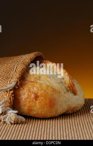 Primo piano di una pagnotta di pane in un sacco di tela su una superficie ondulata e una luce calda scuro dello sfondo. Foto Stock