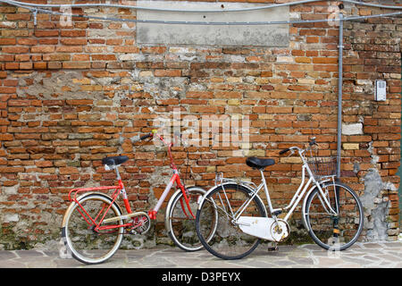 Due biciclette appoggiato uno sbriciolamento rosso parete di mattoni Foto Stock