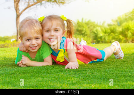 Foto di carino bambina con pretty boy sdraiati sull'erba verde nel parco, allegro bambini in appoggio sul campo Foto Stock