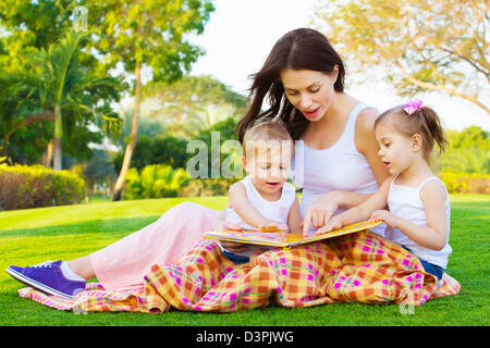 Foto di giovane donna bruna insegnamento due dolci bambini, allegro madre con graziosi la figlia e il figlio incantevole favola di lettura Foto Stock