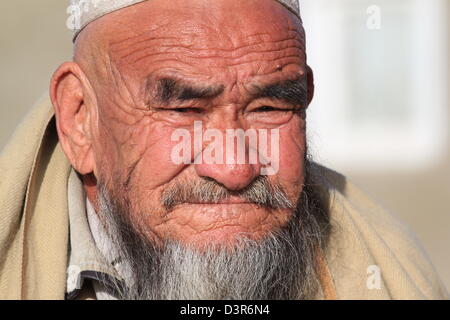 Un vecchio uomo si siede su una parete a Kabul. Il suo volto rigato mostra età avanzata e i suoi occhi squint per vedere attraverso la luce del sole. Foto Stock