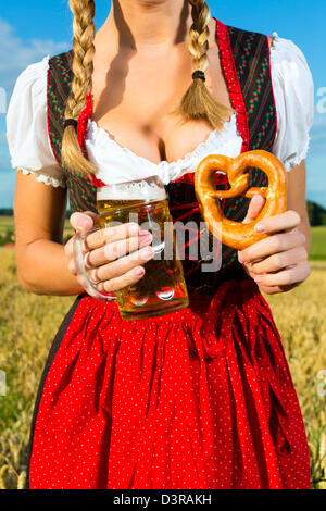 Giovane donna bavarese di bere birra e mantenendo un pretzel in dirndl a prato Foto Stock