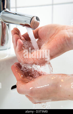 Persona sta lavando le mani sotto l'acqua da un rubinetto in un bagno. Immagine simbolo per lo spreco di acqua. Foto Stock