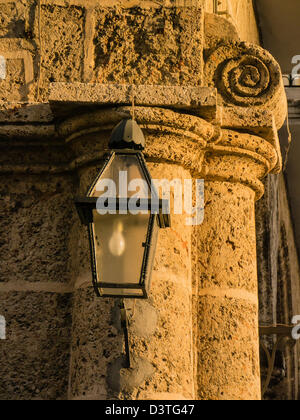 Un nero ferro battuto tradizionale lampada di strada pende da una pietra snocciolate colonna in piazza Duomo, l'Avana, Cuba. Foto Stock