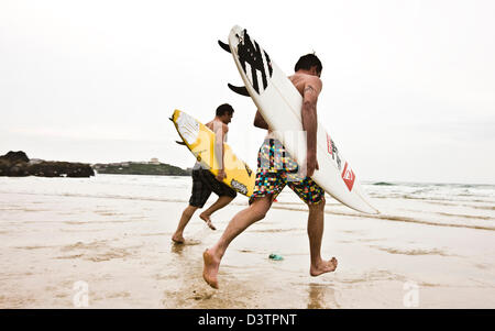 Surfers in esecuzione nel mare freddo, Sant Agnese, Cornwall, Regno Unito Foto Stock