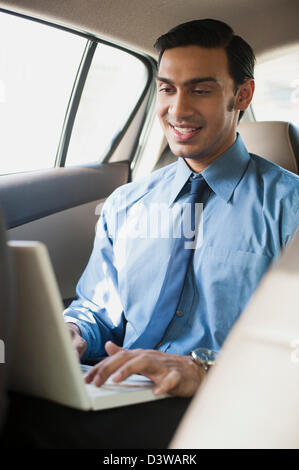 Imprenditore Bengali usando un computer portatile in un'auto Foto Stock