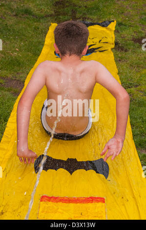 Un dodicenne ragazzo andando verso il basso di uno scivolo d'acqua all'aperto in un giardino nel Regno Unito Foto Stock