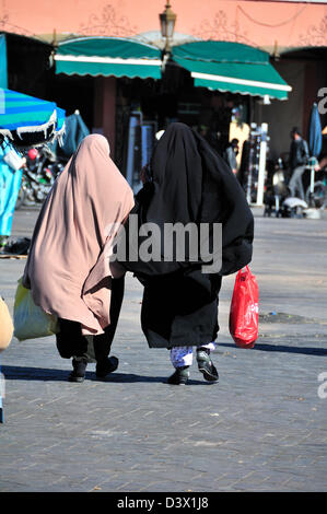 Due donne marocchine indossando l'abaya o abito tradizionale per donne arabe attraversando a piedi la piazza Jemaa El Fna plaza a Marrakech, Marocco Foto Stock