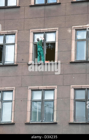 Un pulitore di finestra in piedi sulla sporgenza di finestra di un edificio alto dell'ufficio senza apparecchiatura di sicurezza a riga, Lettonia, Stati baltici Foto Stock