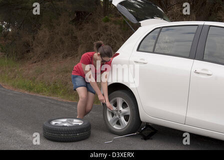 Giovane donna cambia ruota in corrispondenza di una strada in remoto Foto Stock
