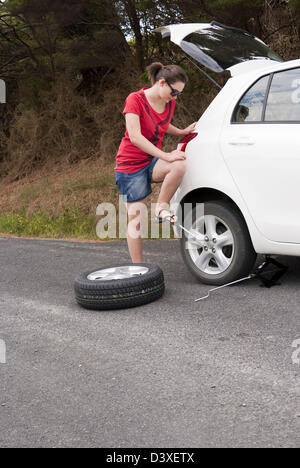 Giovane donna cambia ruota in corrispondenza di una strada in remoto Foto Stock
