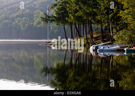 Mattina rompe su vetroso lago ancora, guardando a barche ormeggiate e Muskoka alberi di pino Foto Stock