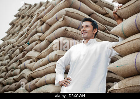 Uomo in piedi accanto alla pila di sacchi di grano, Anaj Mandi, Sohna, Gurgaon, Haryana, India Foto Stock