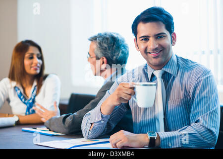 Ritratto di un uomo di affari di bere il caffè con i suoi colleghi a discutere in background Foto Stock