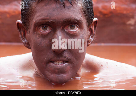 Close up di un uomo immerso nella Red bagno di fango con la sua faccia completamente coperto di fango. Foto Stock