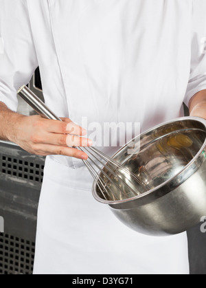 Lo chef con filo Wisk e recipiente di miscelazione Foto Stock