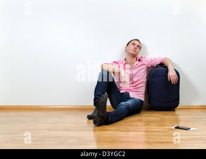 Giovane uomo seduto sul pavimento vicino a valigia Foto Stock